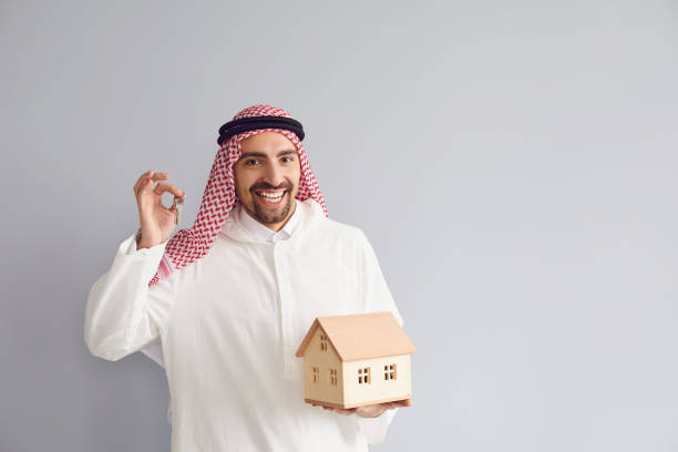 A man in traditional attire holds house keys and a model house, symbolizing Dubai real estate transactions in 2024.