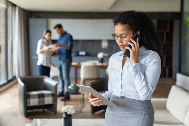 Professional woman making a business call with two colleagues reviewing documents in a modern office setting.